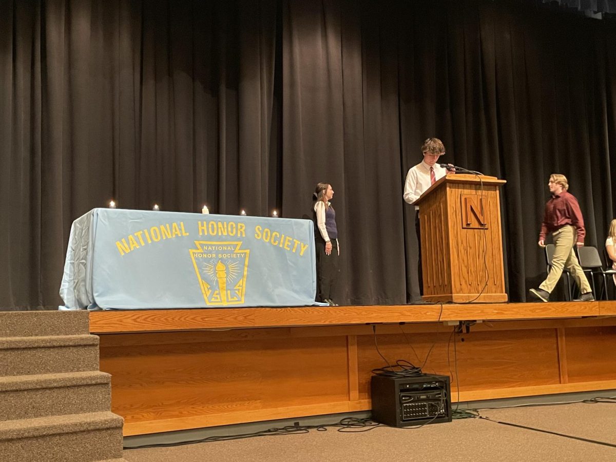 Newly inducted sophomore Christopher Elliott walks across auditorium stage to shake hands with NHS officer Julianne Kellar at the NHS induction ceremony.