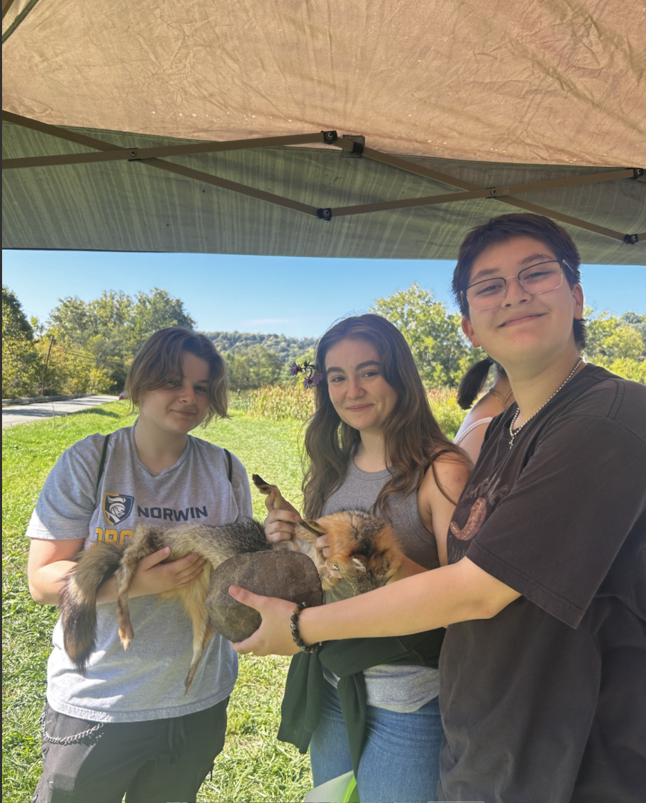 Kayla Lackey, Noelle Kravetz, and Zack Egnitz hold up the hide of a fox at one of the stations. 