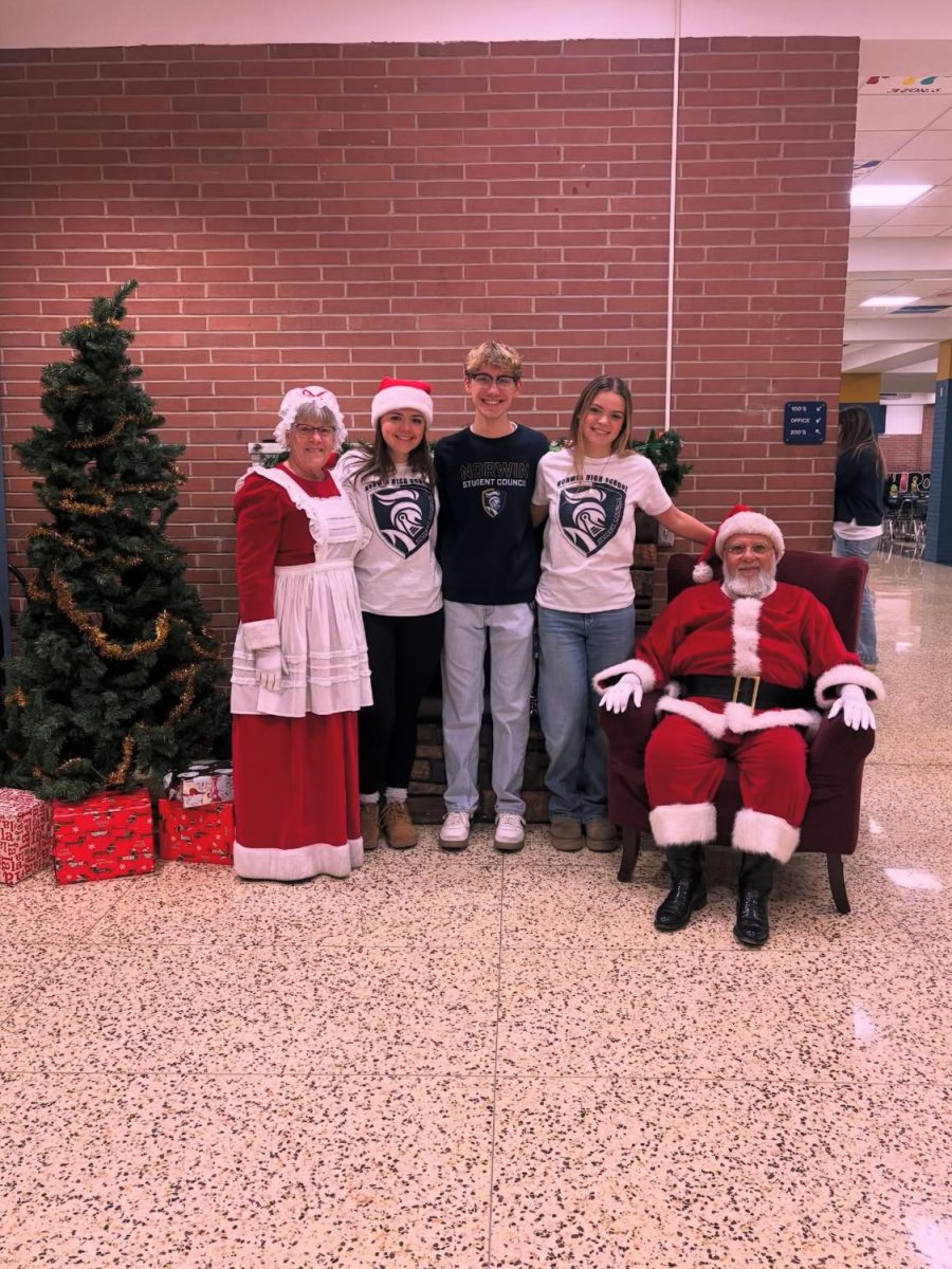 Junior Lydia Dzvonick, junior Ava Bobby, senior Tyler Patrick, Mrs. and Mr. Claus posting for a picture behind the Christmas tree.
